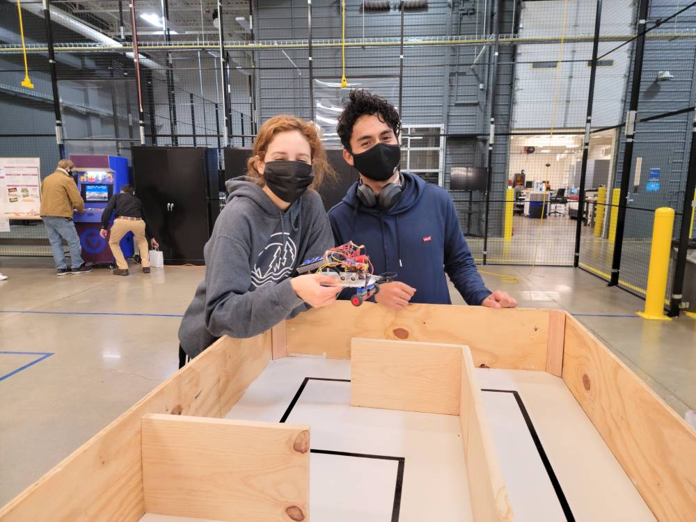 2 people holding a robot over a small maze